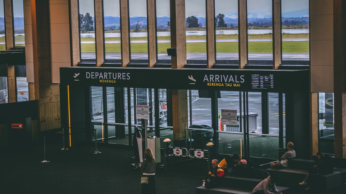 Busy airport terminal area with people, featuring departures and arrivals signs.